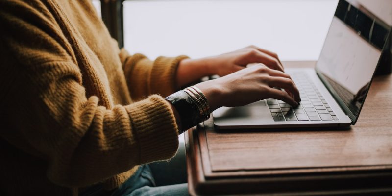 Student writing and typing on a laptop